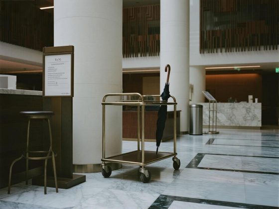 jimeng-2025-07-14-2890-酒店大堂一角，金属行李车、落地指示牌、不锈钢垃圾桶和伞架整齐摆放。空间宽敞，地面...